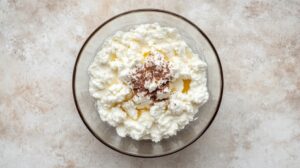 Bowl of ricotta cheese with a drizzle of honey and cocoa powder on top, prepared as ingredients for a dessert
