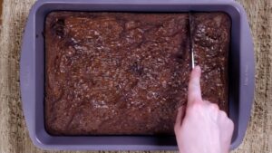 A Person Slices Freshly Baked Nutella Brownies in A Baking Pan with A Crackly Top