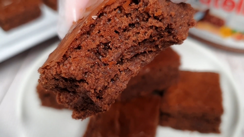 A Close-Up of A Hand Holding a Soft and Fudgy Piece of 3-Ingredient Brownies with A Crackly Top