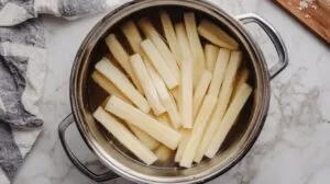 Raw yuca sticks boiling in a large pot of water, viewed from above on a marble countertop