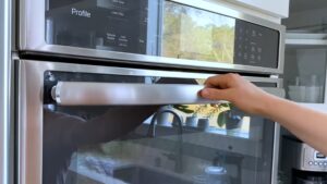 A Hand Is Opening a Modern Stainless Steel Oven in A Bright Kitchen, Preparing to Preheat It