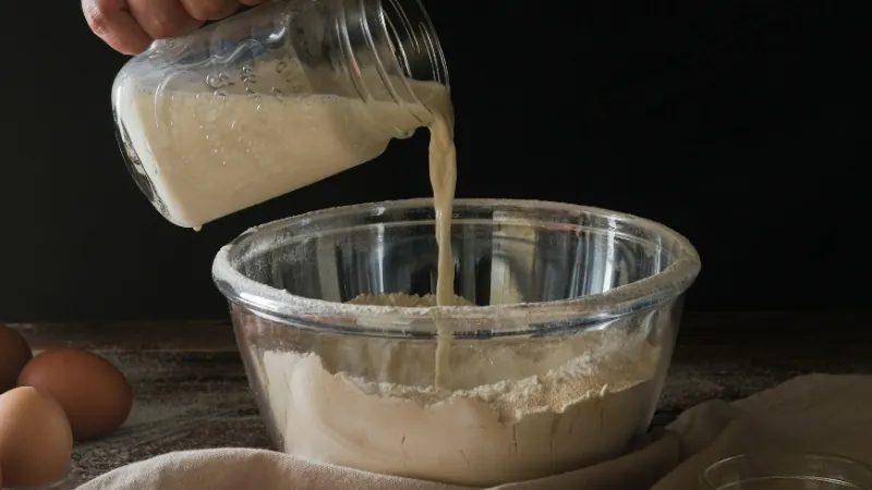 Pouring a buttermilk substitute into a bowl of flour, testing different substitutes for buttermilk in baking