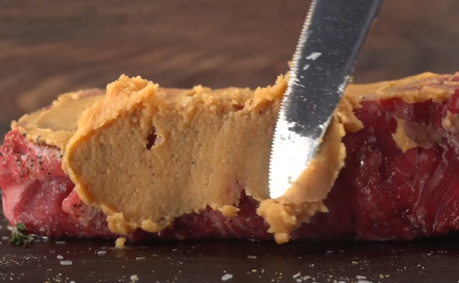 Knife slicing through a flavorful miso spread on a piece of meat
