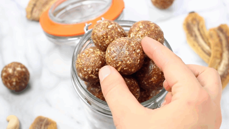 A hand picking up a banana energy bite from a jar filled with no-bake oat and nut balls
