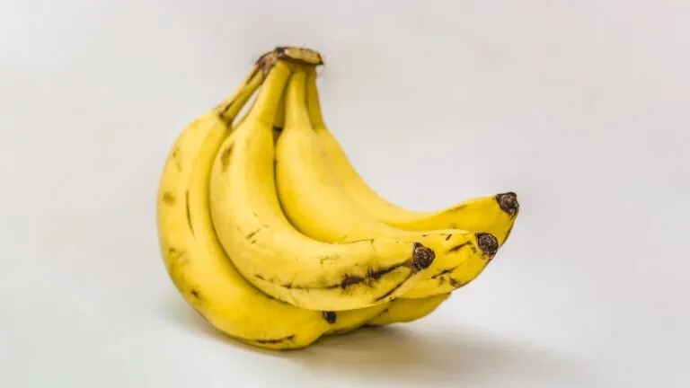 A bunch of ripe bananas with dark spots on their peels sitting on a white surface
