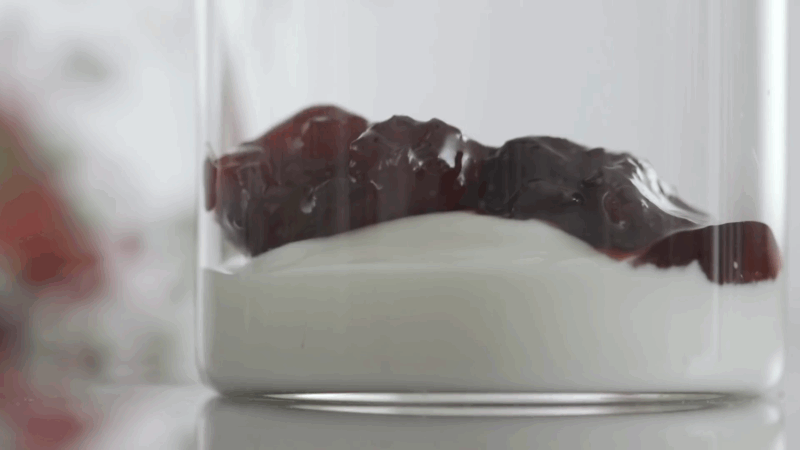 A spoonful of leftover jam or fruit preserves sits on top of plain yogurt in a glass