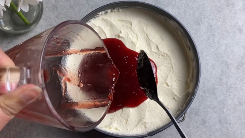 A red fruit preserve mixture is being poured over a creamy mascarpone base for a simple dessert topping