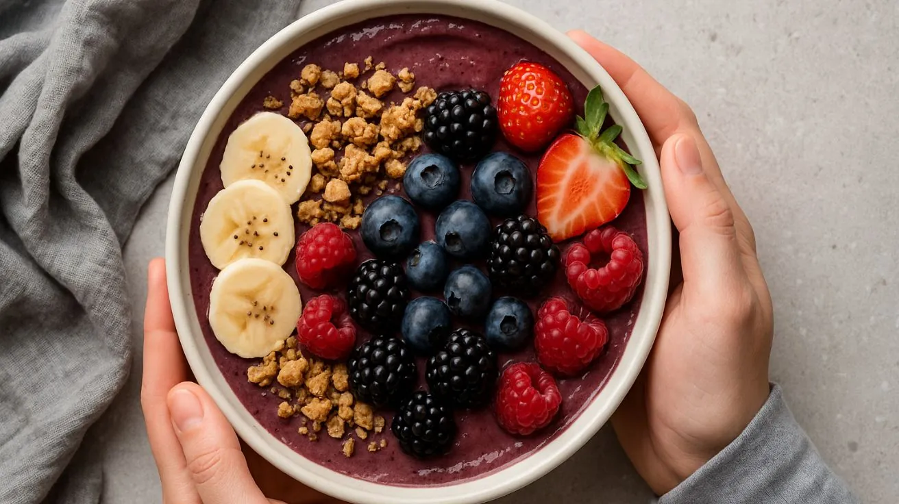 A person holds a white bowl filled with a thick purple acai smoothie, topped with banana slices, granola, blueberries, blackberries, raspberries, and strawberries.