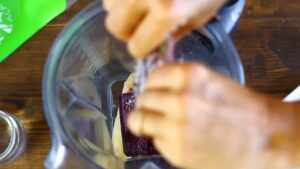 A person adds a chunk of frozen acai into a blender with banana slices already inside