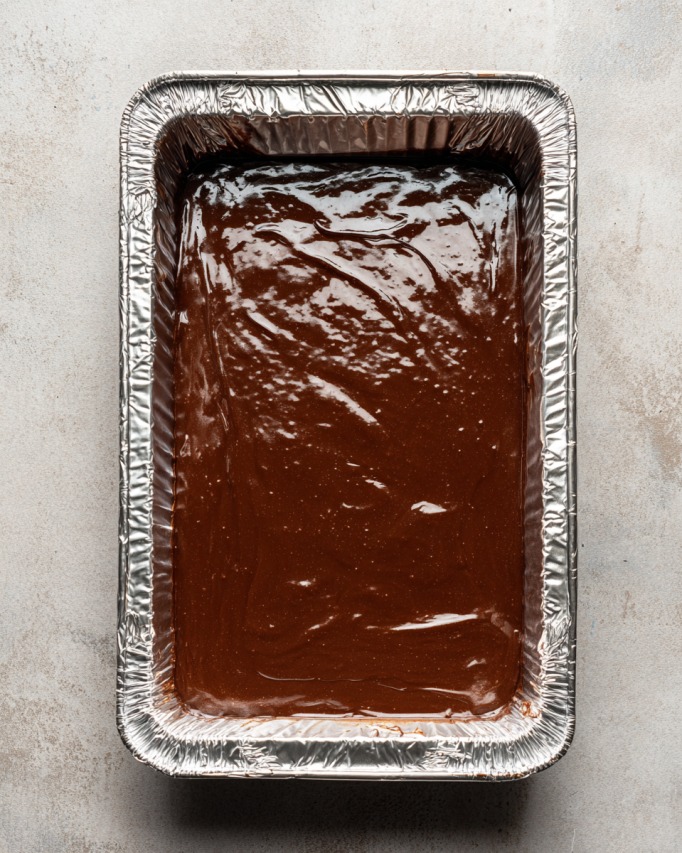 Melted chocolate fudge mixture spread evenly in a foil-lined baking dish