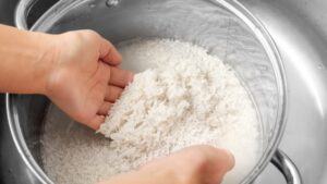 Hands rinsing white rice in a pot of cloudy water over a kitchen sink