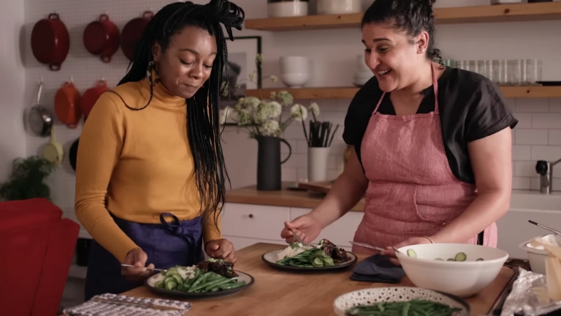 Samin Nosrat shares a meal and a laugh with a guest in a cozy kitchen scene from Salt Fat Acid Heat