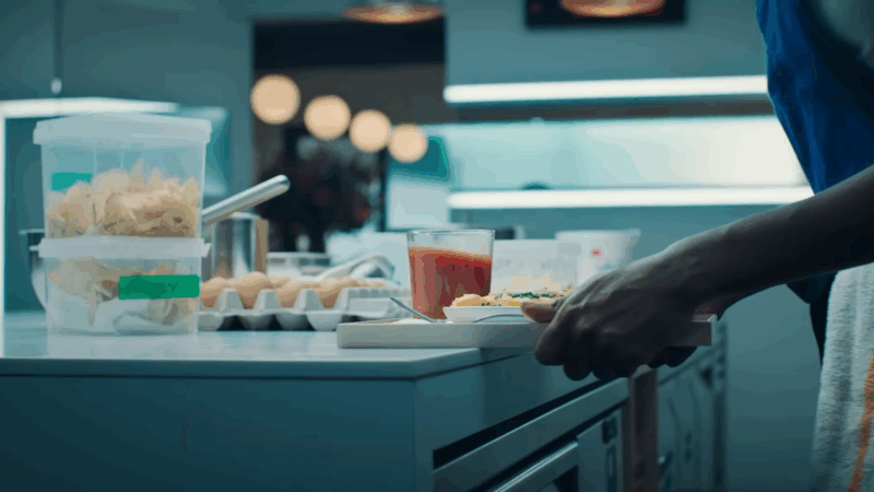 A chef places a finished breakfast dish and drink on the counter in a tense kitchen scene from The Bear