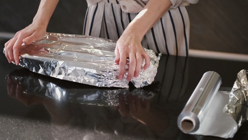 A sheet of aluminum foil is carefully positioned over a baking dish