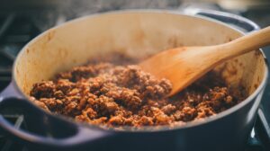 Ground beef browning in a large pot with a wooden spoon, releasing steam as it cooks