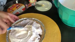 A person is spreading the Kool-Aid pie filling evenly into a graham cracker crust using a spatula