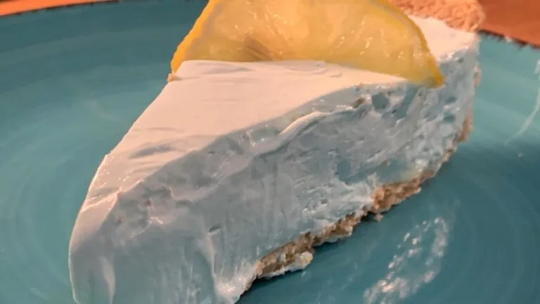 A slice of blue No-Bake Kool-Aid Pie is served on a plate with a lemon wedge on top