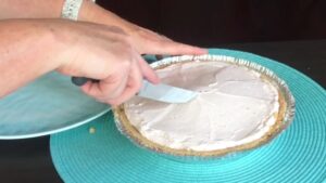 A person is slicing into a chilled Kool-Aid pie with a spatula, ready to serve it